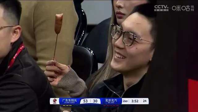 哇塞！真香，宏远把首钢甩开了23分，胡明轩乐得合不拢嘴。

他身后的美女正津津有味地啃着大香肠呢！