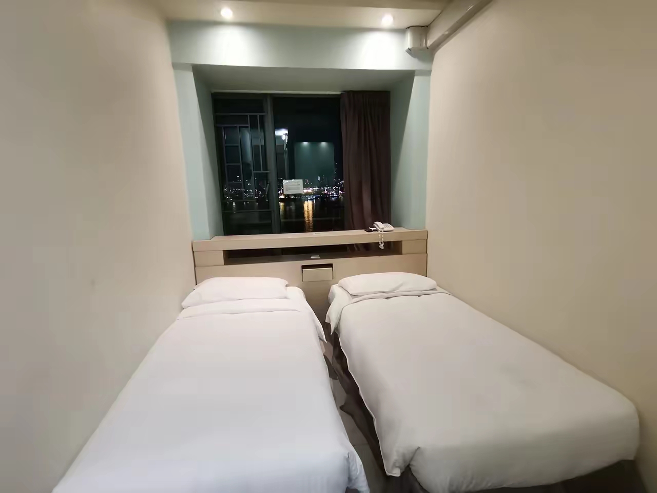 带你看看香港的住宿，狭小，经济，环保，不提供洗漱用具（有2条一次性毛巾），全屋不足8个平方，两个床铺之间是一双鞋子的距离，床头柜是这样的，床铺是这样的，主打一个省钱，实惠——这里是香港葵青区香港永伦8