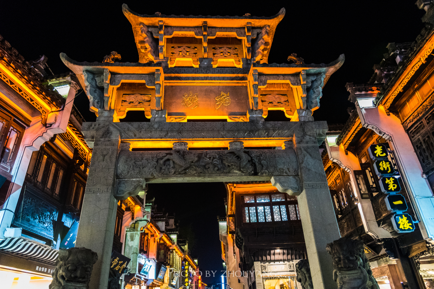 夜晚的屯溪老街，五彩的霓虹装点着鳞次栉比的店铺，粉墙黛瓦的马头墙在夜色下若隐若现，来自全国各地的旅游团与背包客蜂拥的挤进这条并不宽敞的街巷，商家叫唤着买卖，游人目不暇接的走着逛着，路边的餐馆飘出徽菜的