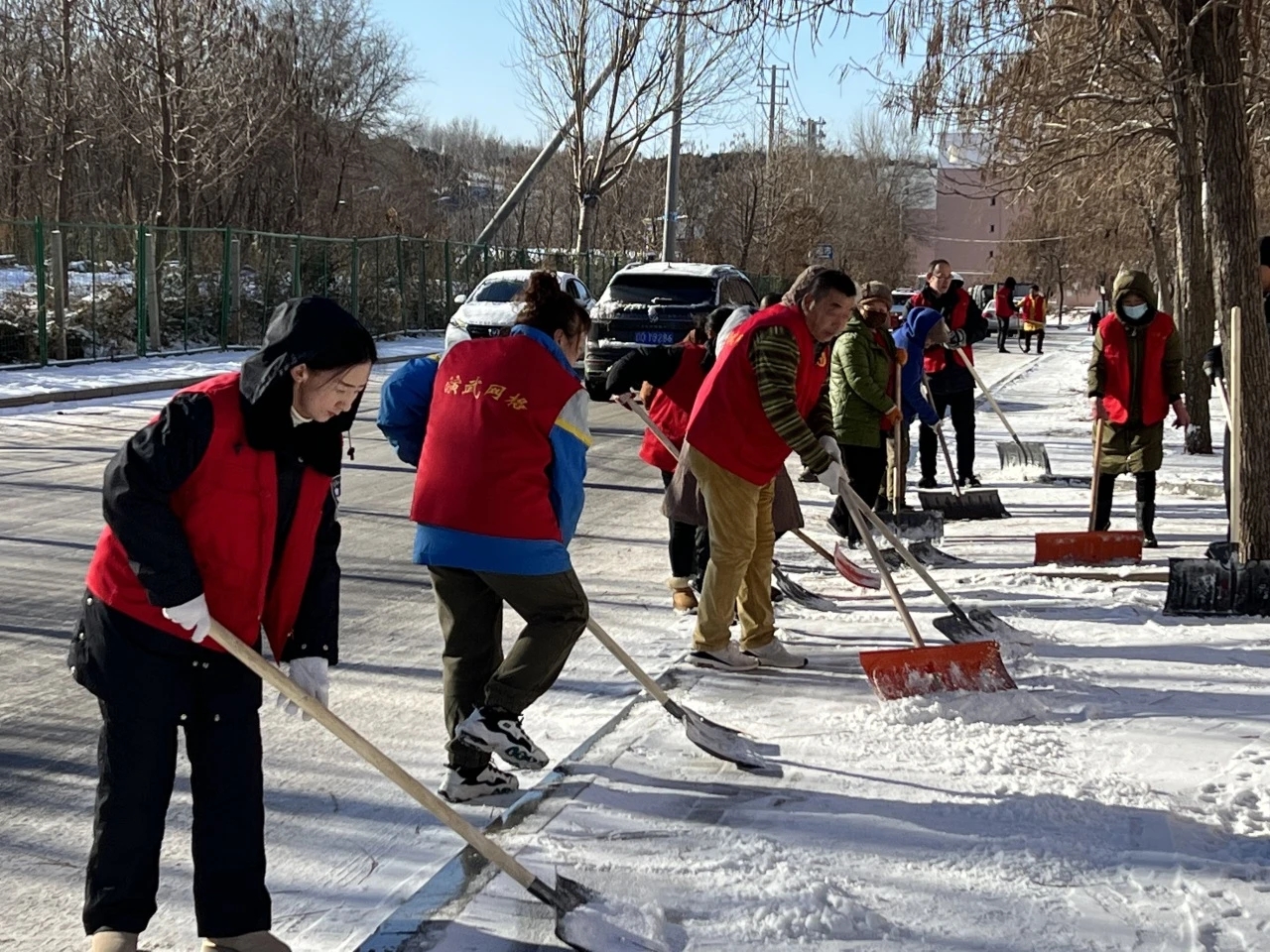 室外扫雪，情暖寒冬。随着冬季的到来，大雪纷飞给社区居民的出行带来了不便，抚顺市望花区演武街道以“雪”为令，组织志愿者们开展扫雪活动。志愿者们身穿红色马甲，手持雪板和铁锹，将社区内的主要道路和背街小巷清